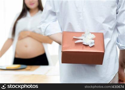 Pregnant woman with husband surprise with gift box - husband holding gift box behind back, celebration family with happy concept.