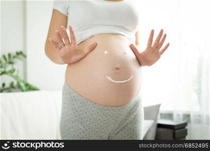 Pregnant woman with smile drawn by creme for stretch marks on tummy