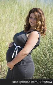pregnant woman with white ribbon bow on her belly in nature with straw background
