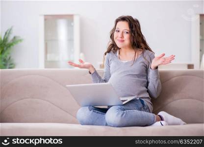 Pregnant woman working on laptop sitting on sofa