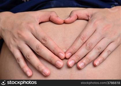 Pregnant women forming a heart with her hands on her belly.