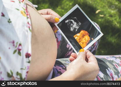 Pregnant women hold picture of womb. Daylight in the garden