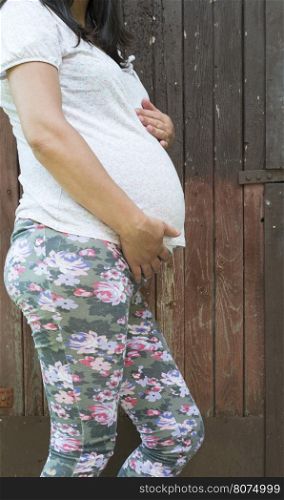 Pregnant women in front of old red wooden wall.