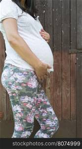 Pregnant women in front of old red wooden wall.