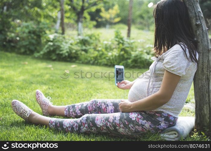Pregnant women with smartphone in a garden