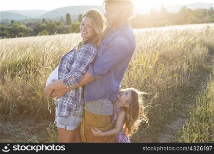 Pregnant young couple and daughter hugging each other in field