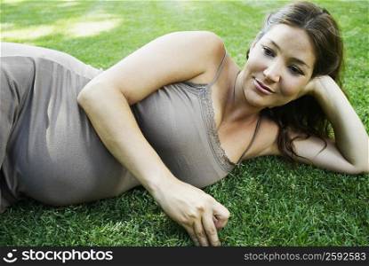 Pregnant young woman lying on the grass and smiling