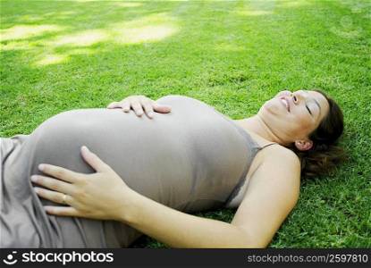 Pregnant young woman lying on the grass and touching her abdomen