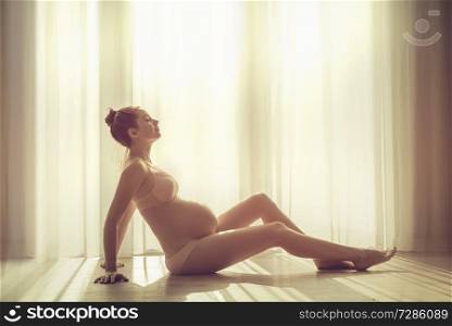 Pregnant young woman over a window background