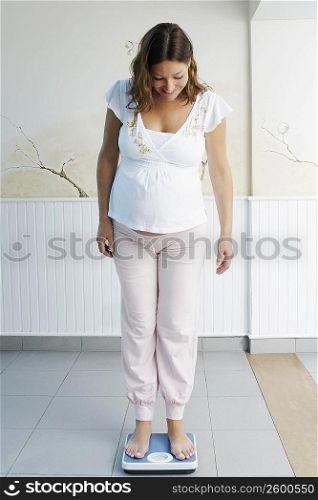 Pregnant young woman standing on a weighing scale