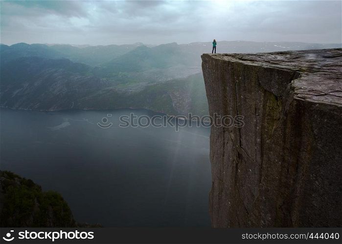 Preikestolen on a overcast day - girl is standing on the edge of a rock in the rain, Norway