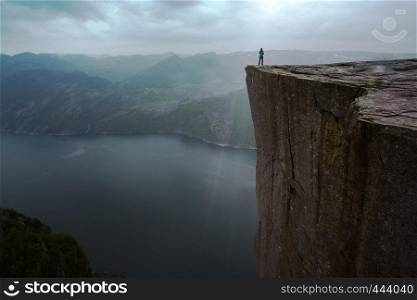 Preikestolen on a overcast day - girl is standing on the edge of a rock in the rain, Norway