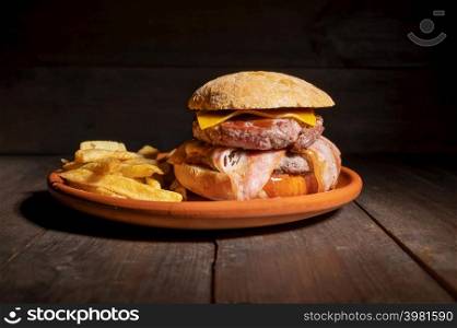 Premium grilled beef hamburger with bacon, cheese and French fries. Delicious American burger on wooden background. High quality photography. Premium grilled beef hamburger with bacon, cheese and French fries. Delicious American burger on wooden background.
