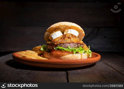 Premium quality Beef burger with goat cheese, caramelized onions in a rustic bun with french fries on the side. Yummy Burger served on a rustic plate on wooden table. High quality photography. Premium quality Beef burger with goat cheese, caramelized onions in a rustic bun with french fries on the side. Yummy Burger served on a rustic plate on wooden table