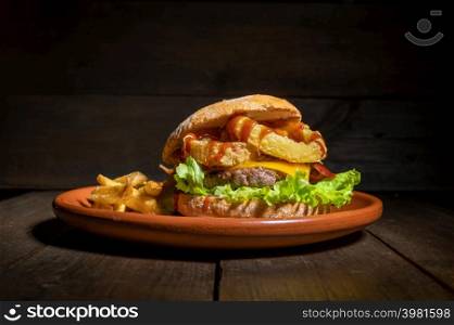 Premium quality burger with onion rings, cheese and barbecue sauce, served with french fries on a rustic plate. High quality photography.. Premium quality burger with onion rings, cheese and barbecue sauce, served with french fries on a rustic plate