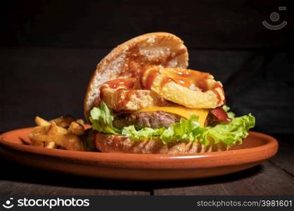 Premium quality burger with onion rings, cheese and barbecue sauce, served with french fries on a rustic plate. High quality photography.. Premium quality burger with onion rings, cheese and barbecue sauce, served with french fries on a rustic plate