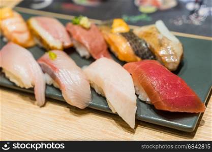 Premium Sushi Set Include Engawa, Hamachi, Hotate, Toro, Roasted Duck, Salmon, Sea Urchin and Tai Served with Wasabi and Curly Green Onion Garnish on The Black Stone Plate.