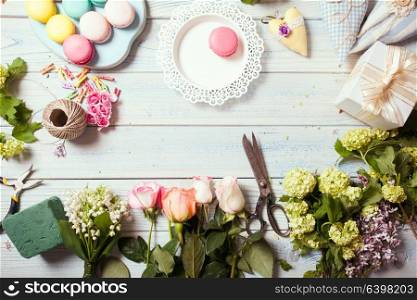 Preparation of flower box with macaroons, top view of florist workplace. Box with flowers and macaroons