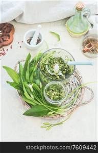 Preparation of green wild garlic pesto making on white kitchen table with ingredients. Top view. Seasonal home cuisine. Vegan food. Healthy cooking and eating