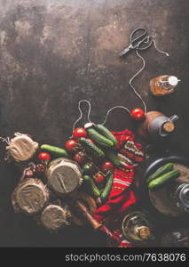 Preparation of homemade pickled cucumbers in jars with scissors, cord, red kitchen towel, oil, vegetables. Rustic autumn concept on dark background. Top view. Border