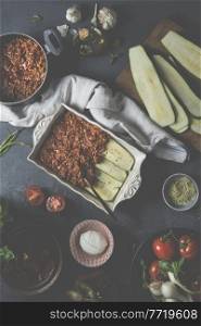 Preparation of Lasagne with zucchini and bolognese sauce on a rustic dark table with various ingredients  mozzarella cheese, ingredients, fresh vegetables and olive oil. View from above. Cook at home