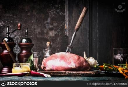 Preparation of raw pork ham meat on rustic kitchen table at dark wooden background, side view