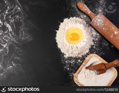 Preparation of the dough. The rolling pin with flour on a dark background. Free space for text.. Rolling pin and white flour on a dark background