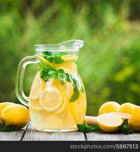 Preparation of the lemonade drink. Lemonade in the jug and lemons with mint on the table outdoor. Lemonade in the jug