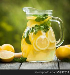 Preparation of the lemonade drink. Lemonade in the jug and lemons with mint on the table outdoor. Lemonade in the jug