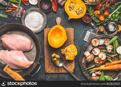 Preparation with Pumpkin , vegetables and mushrooms ingredients with Chicken breast in cooking pot, dark rustic background, top view