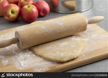 Preparing fresh dough with a wooden rolling pin and flour for baking an apple pie close up