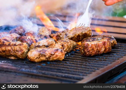 Preparing meat rolls called mici or mititei on barbecue. close up of grill with burning fire with flame and smoke.