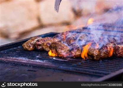 Preparing meat rolls called mici or mititei on barbecue. close up of grill with burning fire with flame and smoke.