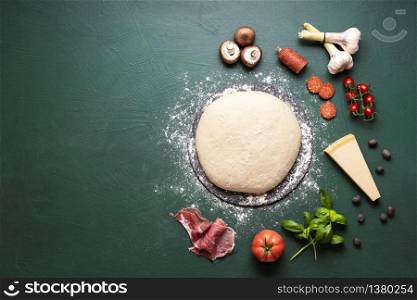 Preparing pizza context with pizza dough and ingredients on a green background. Top view of pizza ingredients and dough. Making italian pizza recipe.