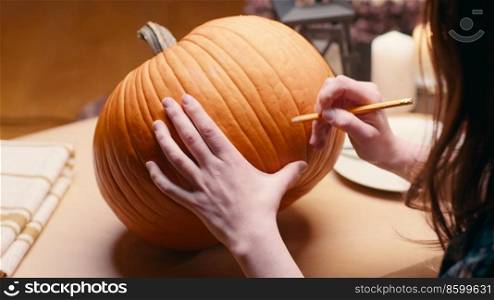 Preparing pumpkin for Halloween. Woman sitting and marking pumpkin with pencil before carving halloween Jack O Lantern at home for her family.. Woman carving Jack O Lantern pumpkin for Halloween