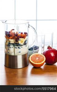 Preparing smoothies with fruit and yogurt. Healthy smoothie ingredients in blender with fresh fruit ready to blend on kitchen table