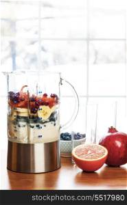Preparing smoothies with fruit and yogurt. Healthy smoothie ingredients in blender with fresh fruit ready to blend on kitchen table
