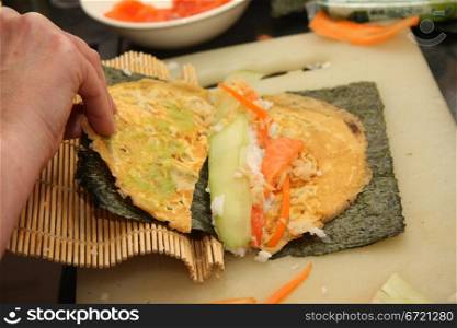 Preparing sushi: rolling rice, egg and fish in seaweed