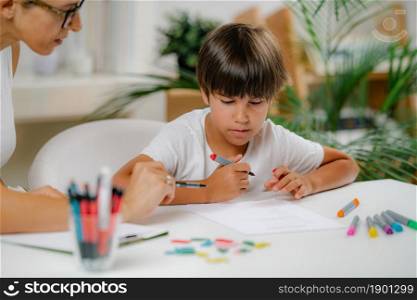 Preschool boy doing school education assessment test. Psychologist asking a questions and preschool boy writing answers.