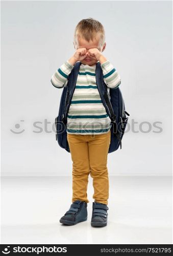 preschool education and childhood concept - crying little boy with school backpack over grey background. crying little boy with school backpack