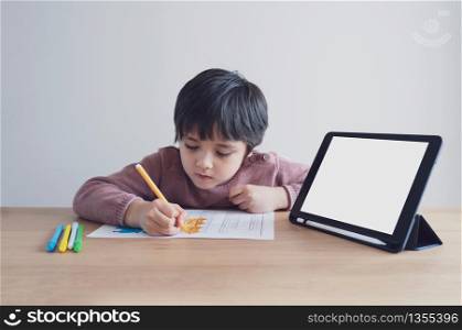 Preschool kid using tablet for his homework,Child wearing head phone doing homework by using digital tablet searching information on internet,Home schooling education concept,Social Distancing