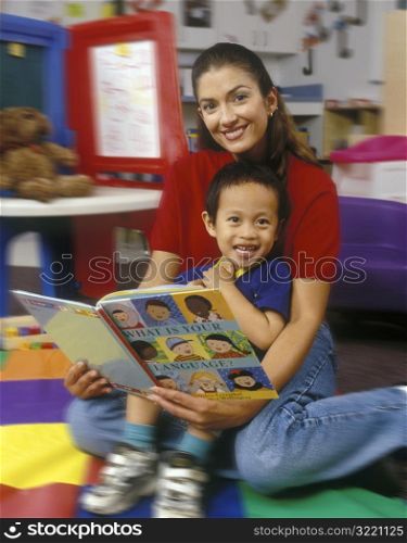 Preschool Teacher Reading Language Book With Asian American Boy