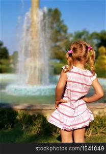 Preschooler little girl watching fountain rear view. Young female child enjoy being outside in summertime. Curiosity blonde looking at splashing droplets. enjoyment of holidays. Pretty kid photography