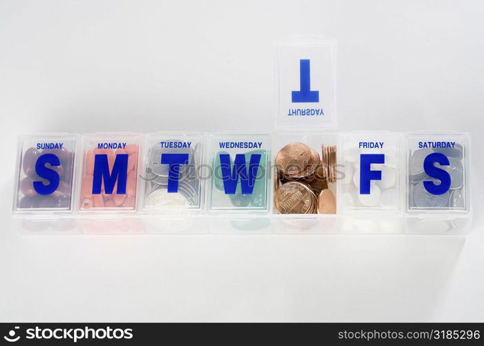 Prescription medication schedule box containing coins and capsules