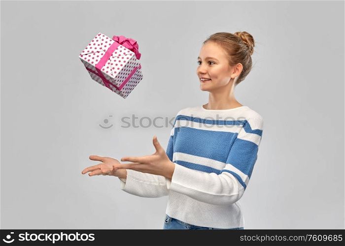 present, greeting and people concept - smiling teenage girl in pullover with gift box over grey background. smiling teenage girl in pullover with gift box