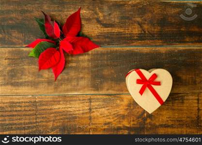 Present with heart shape and seasonal plant with red leaves on a wooden background