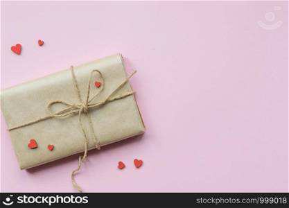 Present wrapped in brown craft paper and tie hemp string on Light pink background. Gift box with decorative red hearts for Mothers Day, Wedding, Birthday and Valentines Day. Top view. Copyspace. Present wrapped in brown craft paper and tie hemp string on Light pink background. Romantic Gift with decorative red hearts. Top view.