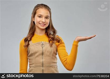 presentation and people concept - happy smiling young teenage girl holding something on empty hand over grey background. happy teenage girl holding something on empty hand