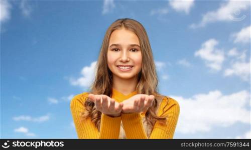 presentation and people concept - happy smiling young teenage girl holding something on empty hands over blue sky and clouds background. teenage girl holding something on empty hands