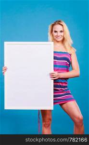 Presenting advertisement concept. Happy positive blonde woman wearing colorful short dress holding blank white board. Happy positive blonde woman holding blank white board